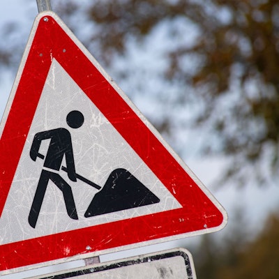 Das Foto zeigt ein zerkratztes Schild mit dem Piktogramm eines Bauarbeiters zur Beschilderung einer Baustelle.