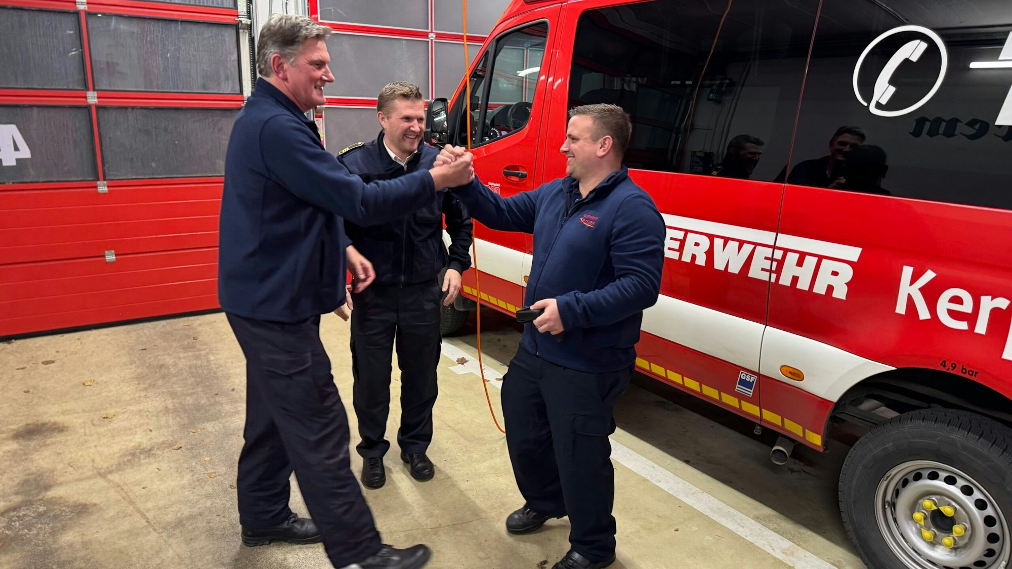Das Foto zeigt drei Männer von der Feuerwehr vor einem Einsatzwagen.