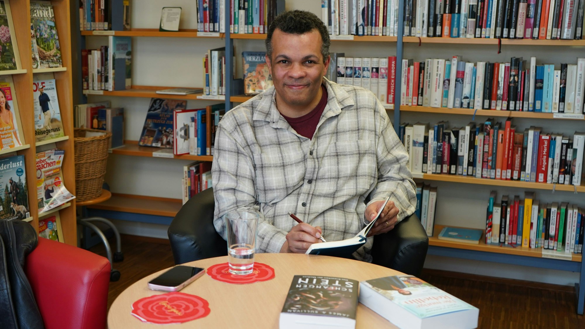 Das Foto zeigt einen Mann, der vor Büchern sitzt und in ein Notizbuch schreibt.