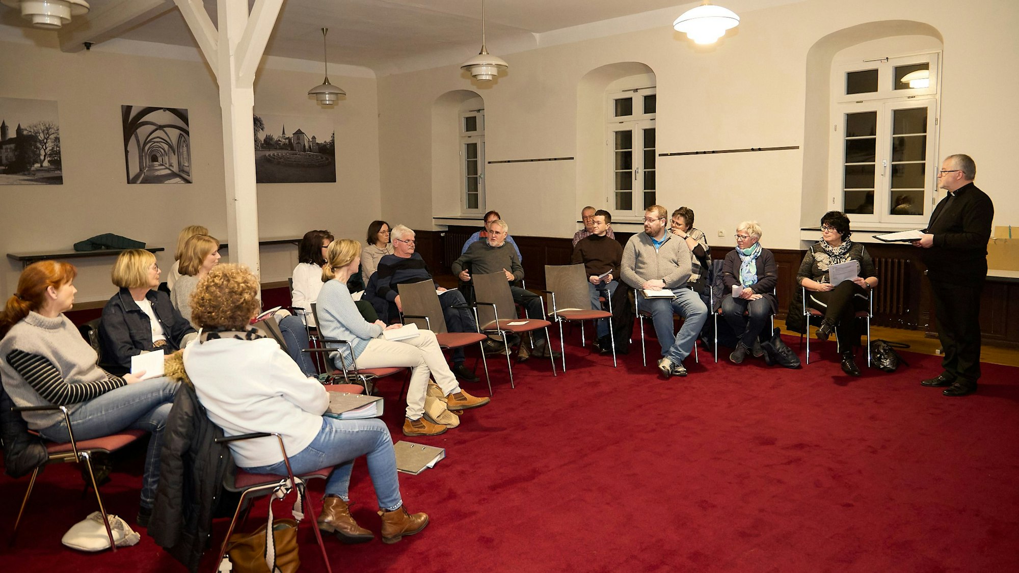 Einige Männer und Frauen sitzen im Halbkreis auf Stühlen, rechts steht der Steinfelder Pfarrer Wieslaw Kaczor.