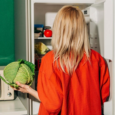 Eine Frau steht vor dem Kühlschrank und hält einen kohl in der Hand.