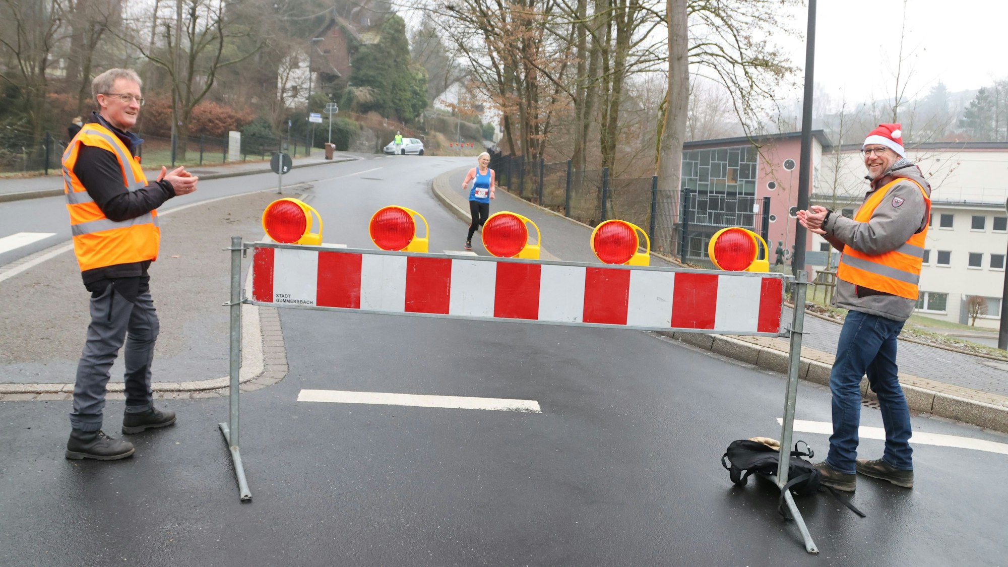 Zwei Männer stehen an einer Straßensperrung bei einer Laufveranstaltung.