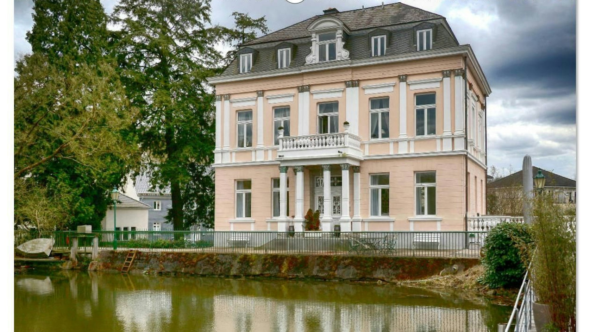 Ein schönes, altes Herrenhaus vor einem Fluss ist zu sehen.