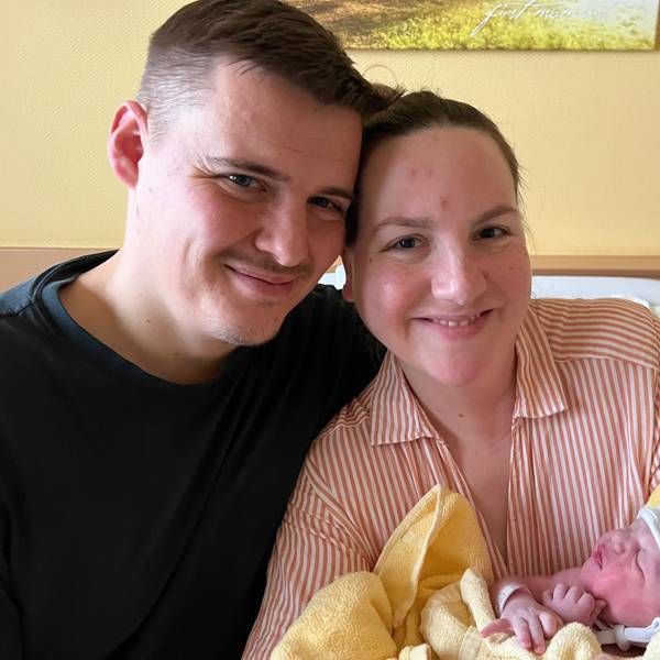 Auf dem Bild sind eine Mutter und ein Vater mit ihrer neugeborenen Tochter zu sehen.