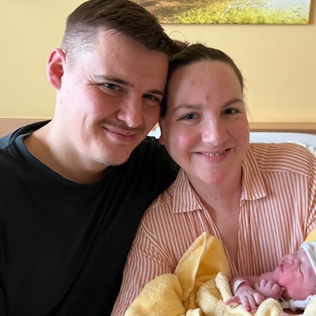 Auf dem Bild sind eine Mutter und ein Vater mit ihrer neugeborenen Tochter zu sehen.