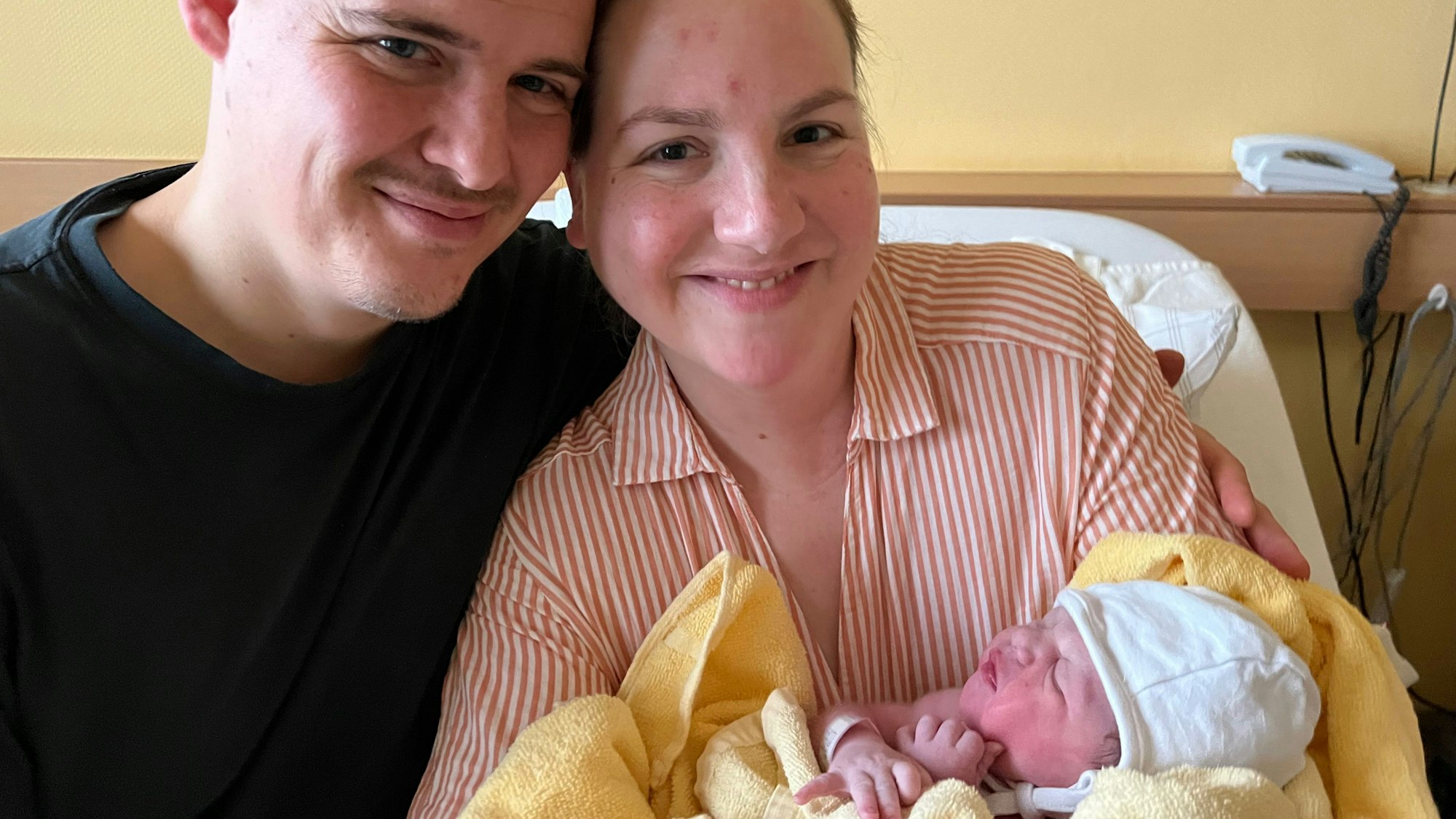 Auf dem Bild sind eine Mutter und ein Vater mit ihrer neugeborenen Tochter zu sehen.