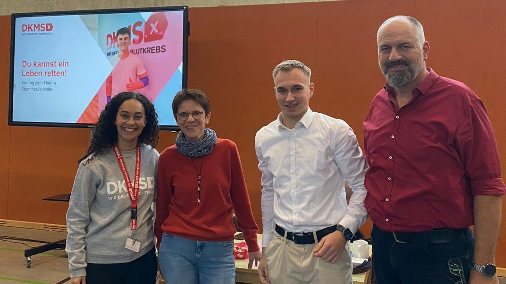 Salome Steinhoff, Birgit Karsten, Tim Förster und Klaus Drotbohm stehen nebeneinander. Links hinter ihnen ist ein Plakat der DKMS zu sehen.