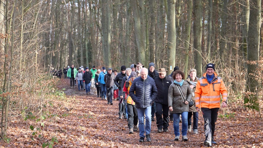 Eine große Gruppe Menschen geht durch den winterlichen Wald.