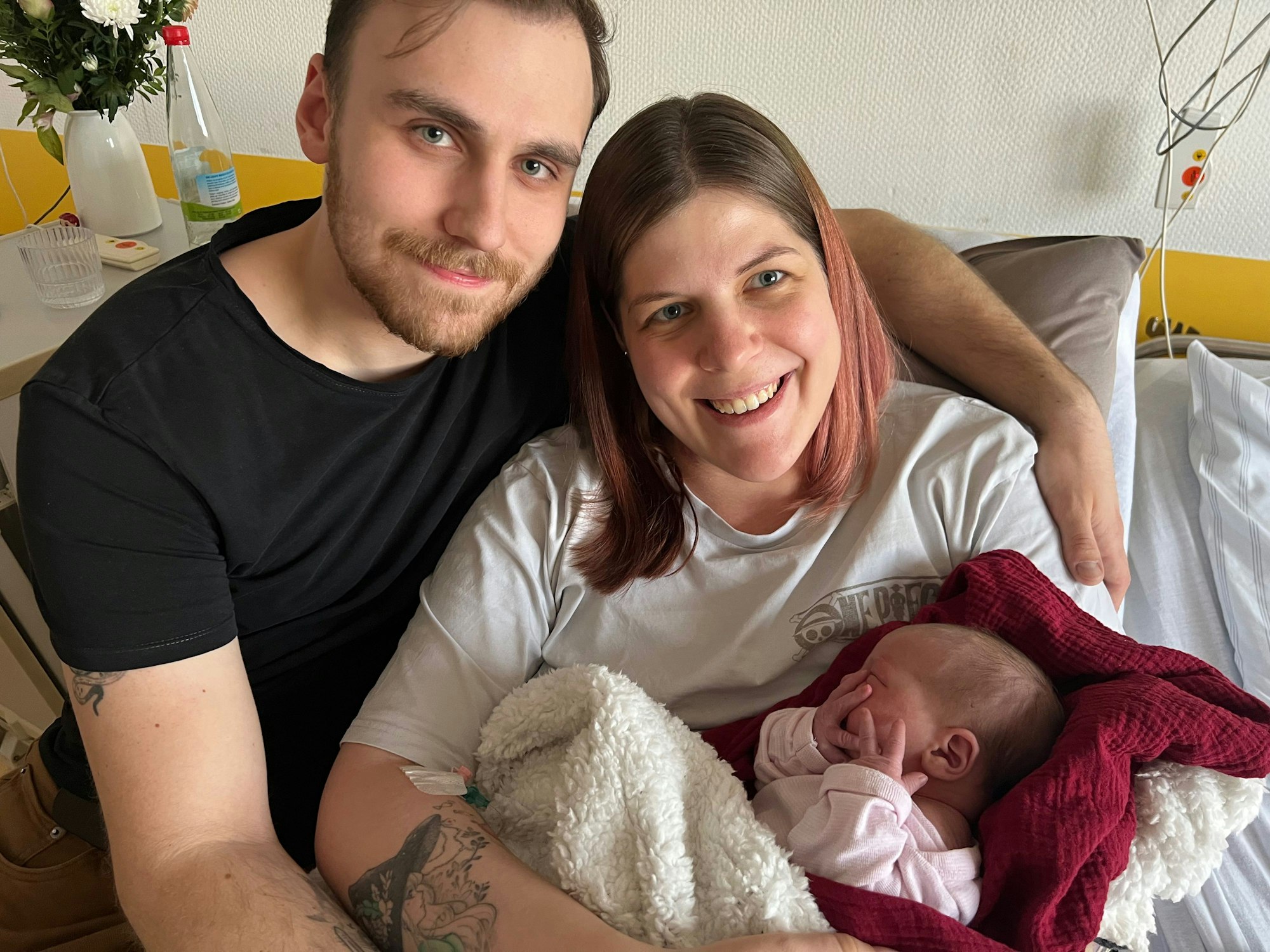 Auf dem Bild ist ein Elternpaar mit seiner neugeborenen Tochter zu sehen.