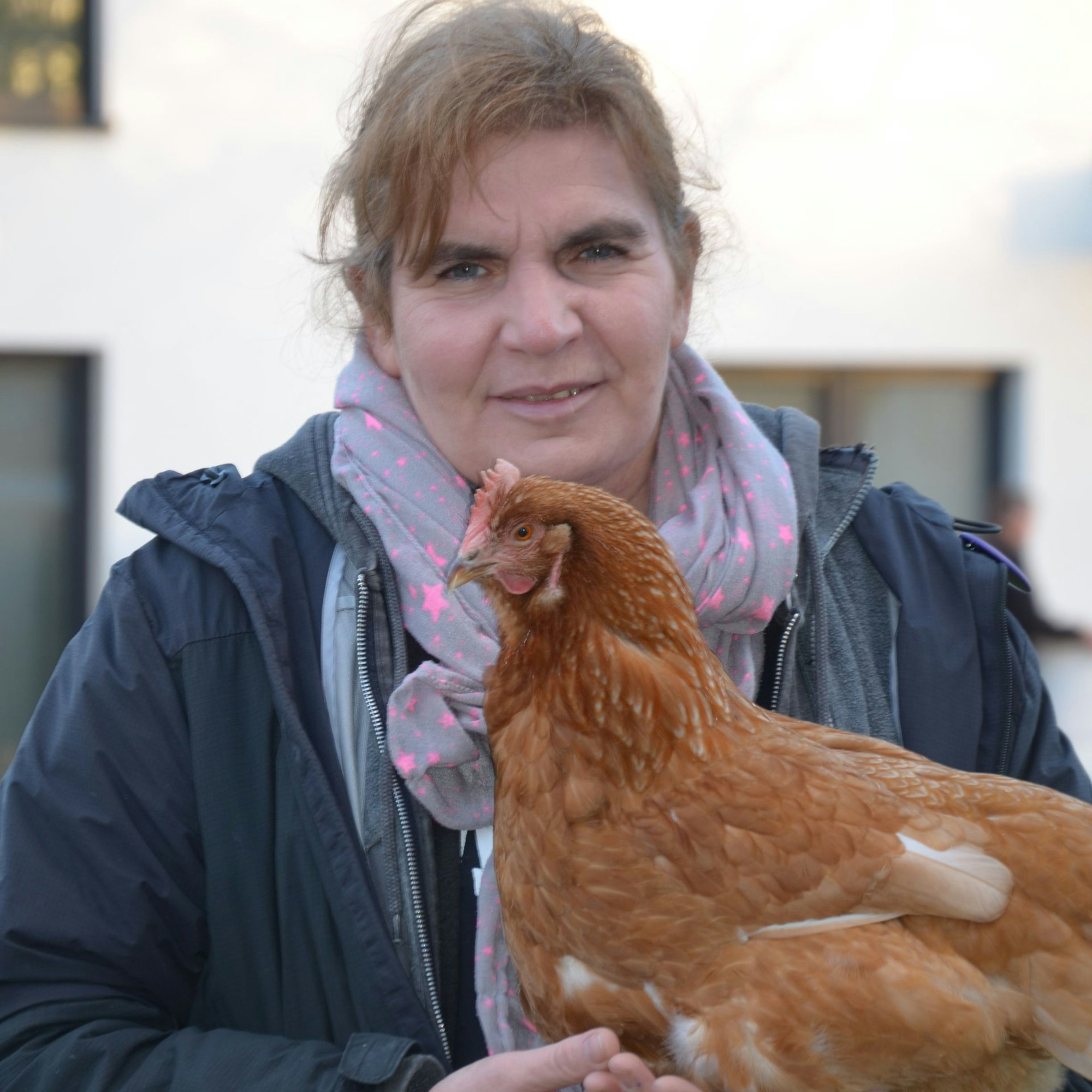 Auf dem Bild ist eine Frau zu sehen, die ein braunes Huhn auf dem Arm hält.