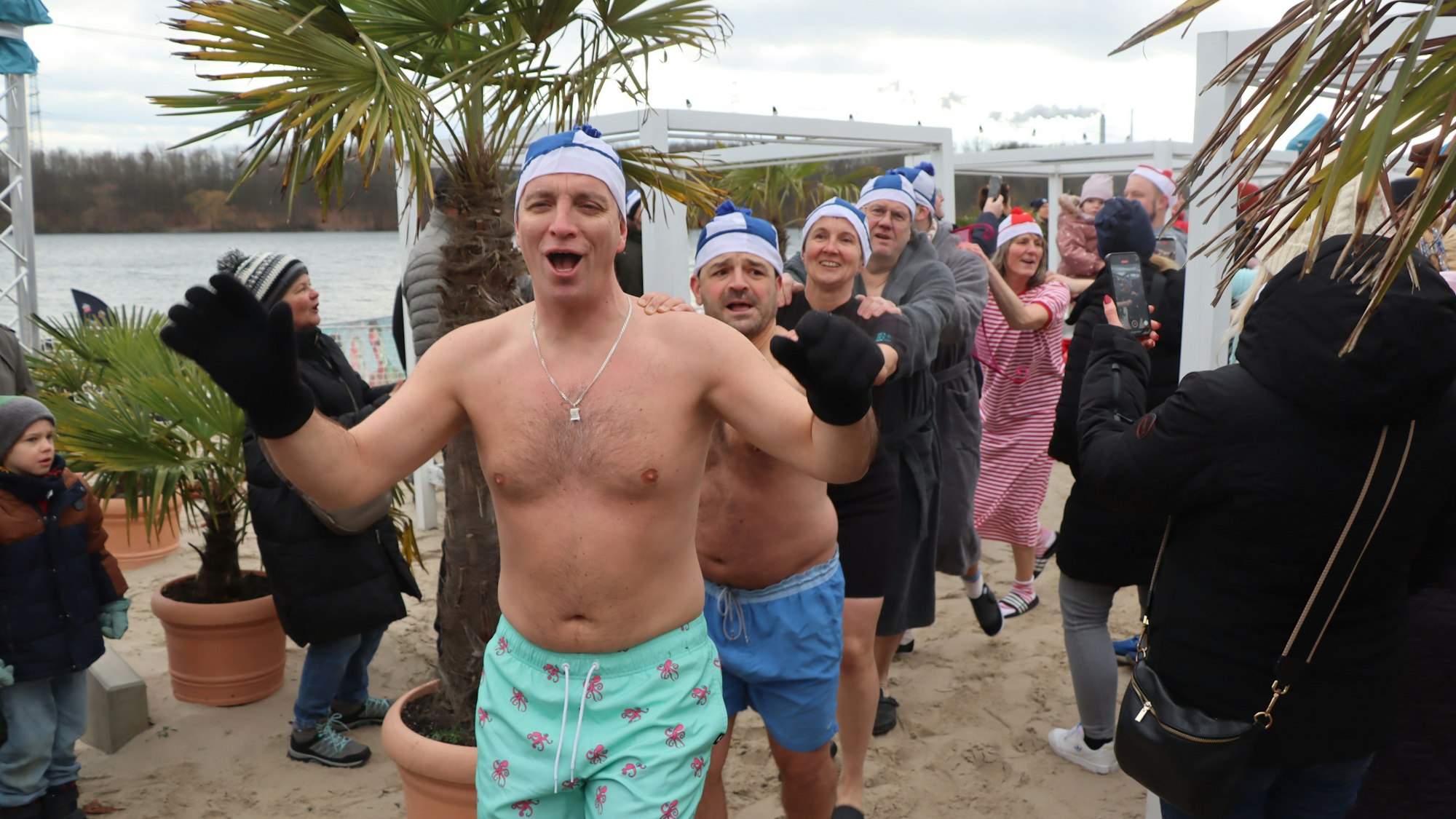 Auf dem Bild sind Teilnehmer des Schwimmens in Badehose zu sehen, die sich in einer Polonaise warm tanzen.