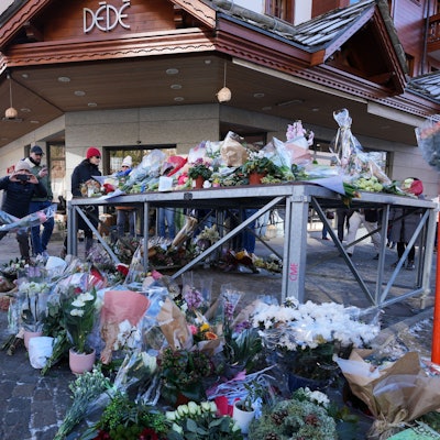 Das Bild zeigt Menschen, die Blumen und Briefe in die Nähe der abgeriegelten Bar Le Constellation, wo ein verheerendes Feuer während der Silvesterfeierlichkeiten in Crans-Montana in den Schweizer Alpen Tote und Verletzte forderte, ablegen. Foto: Antonio Calanni/AP/dpa