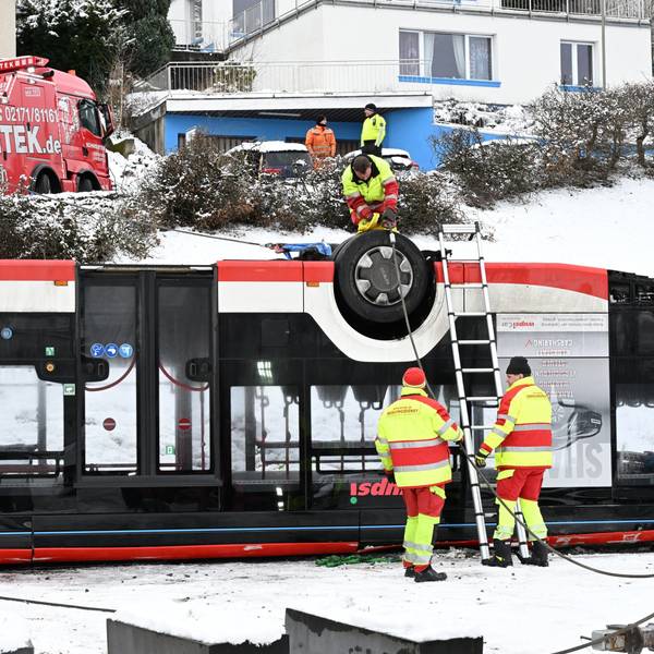 Der Bus liegt auf dem Dach. Zwei Mitarbeiter des Bergungstrupps begutachten das Wrack.