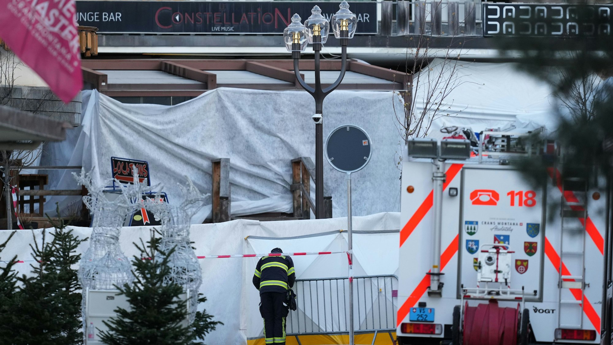 Das Bild zeigt einen Feuerwehrmann der die abgeriegelte Bar Le Constellation, in der ein verheerendes Feuer während der Silvesterfeierlichkeiten in Crans-Montana in den Schweizer Alpen Tote und Verletzte forderte, beobachtet. Foto: Antonio Calanni/AP/dpa