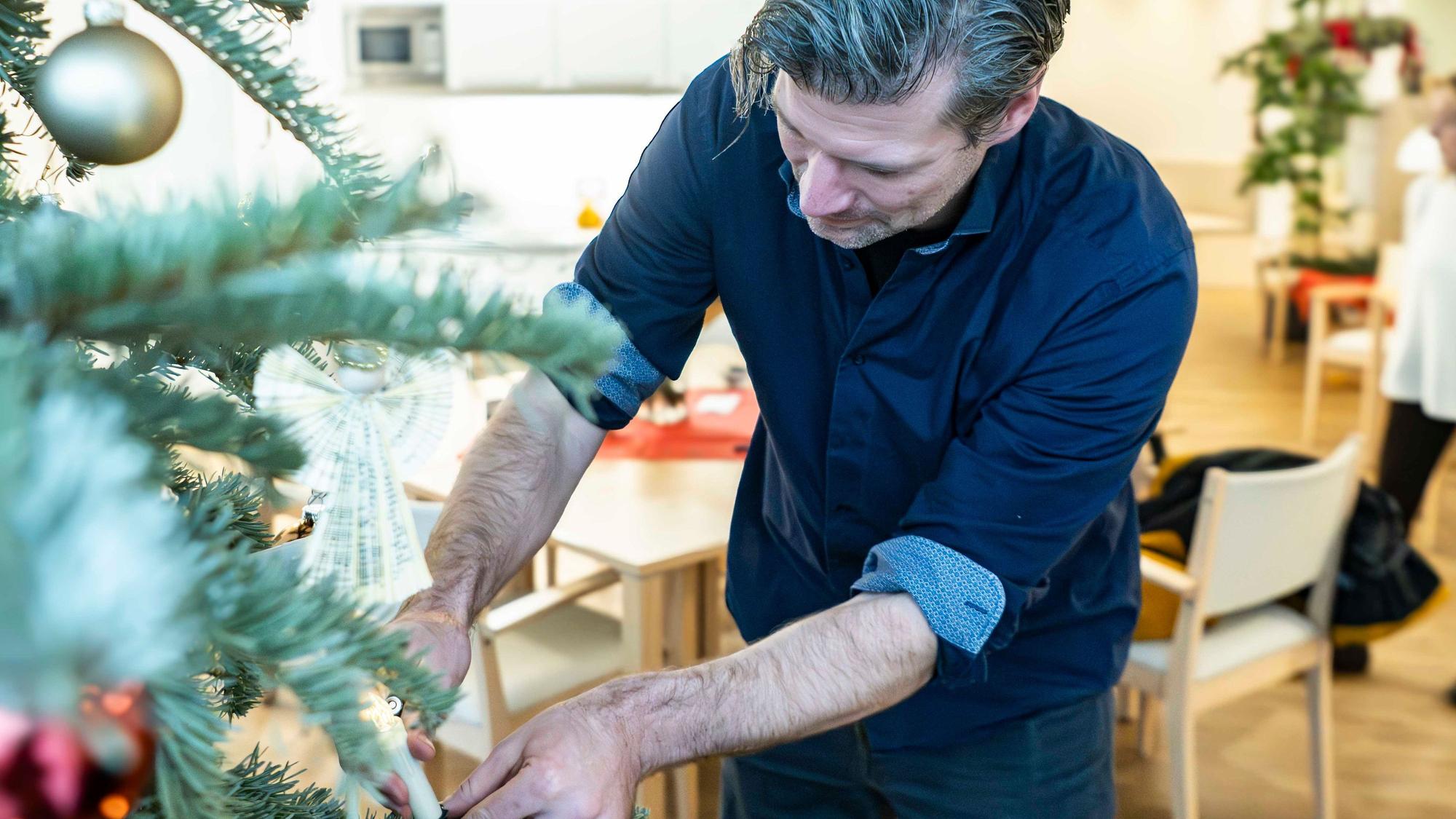 Das Bild zeigt den Leiter der Einrichtung, während er am Weihnachtsbaum die Batterie einer Kerze wechselt.