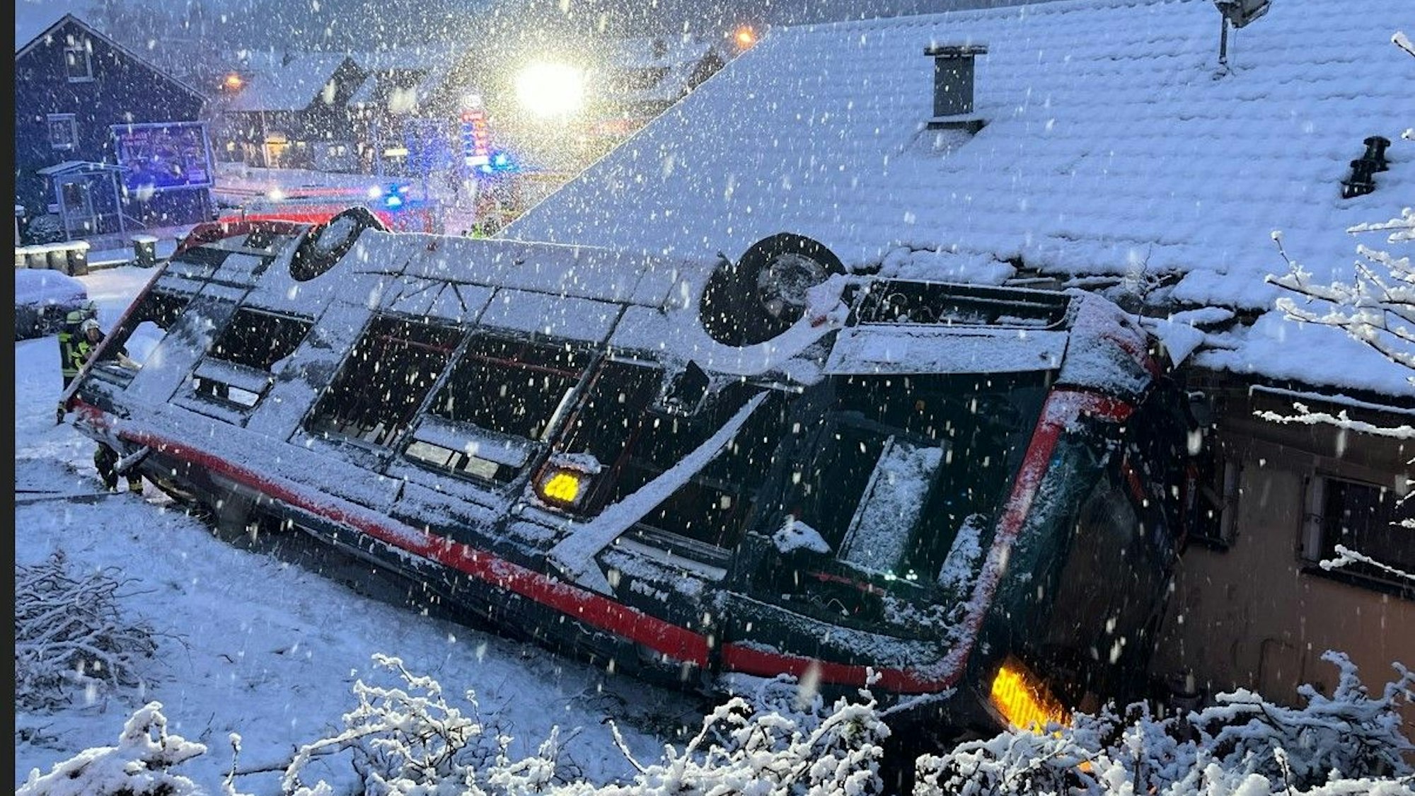 Ein Bus steht auf dem Dach an eine Häuserwand gelehnt. Drum herum liegt Schnee.