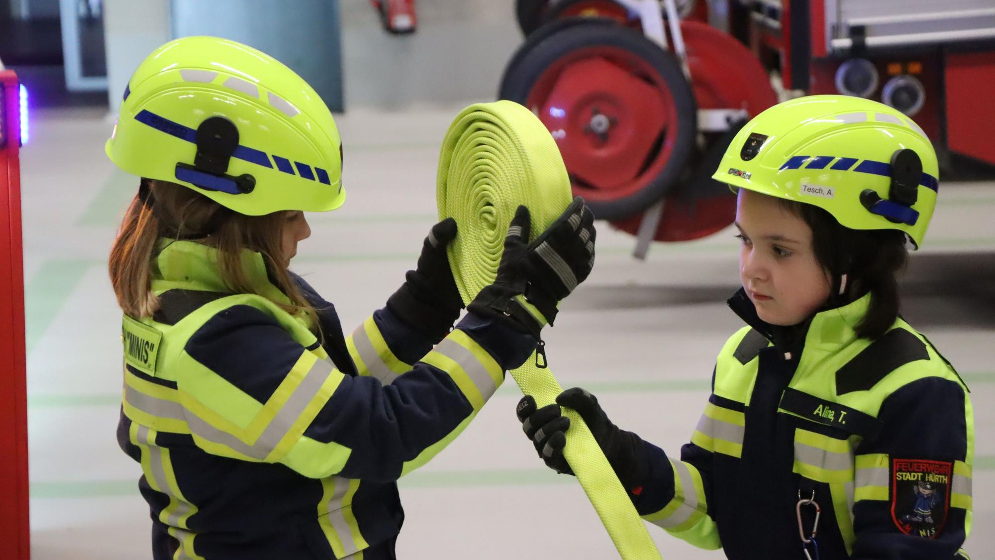 Kinder rollen einen Feuerwehrschlauch auf.