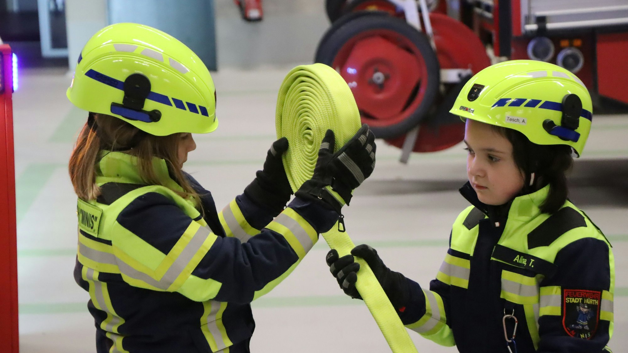 Kinder rollen einen Feuerwehrschlauch auf.