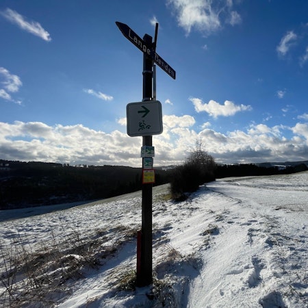 Blick auf die schneebedeckten Flächen und auf einen Wegweiser.