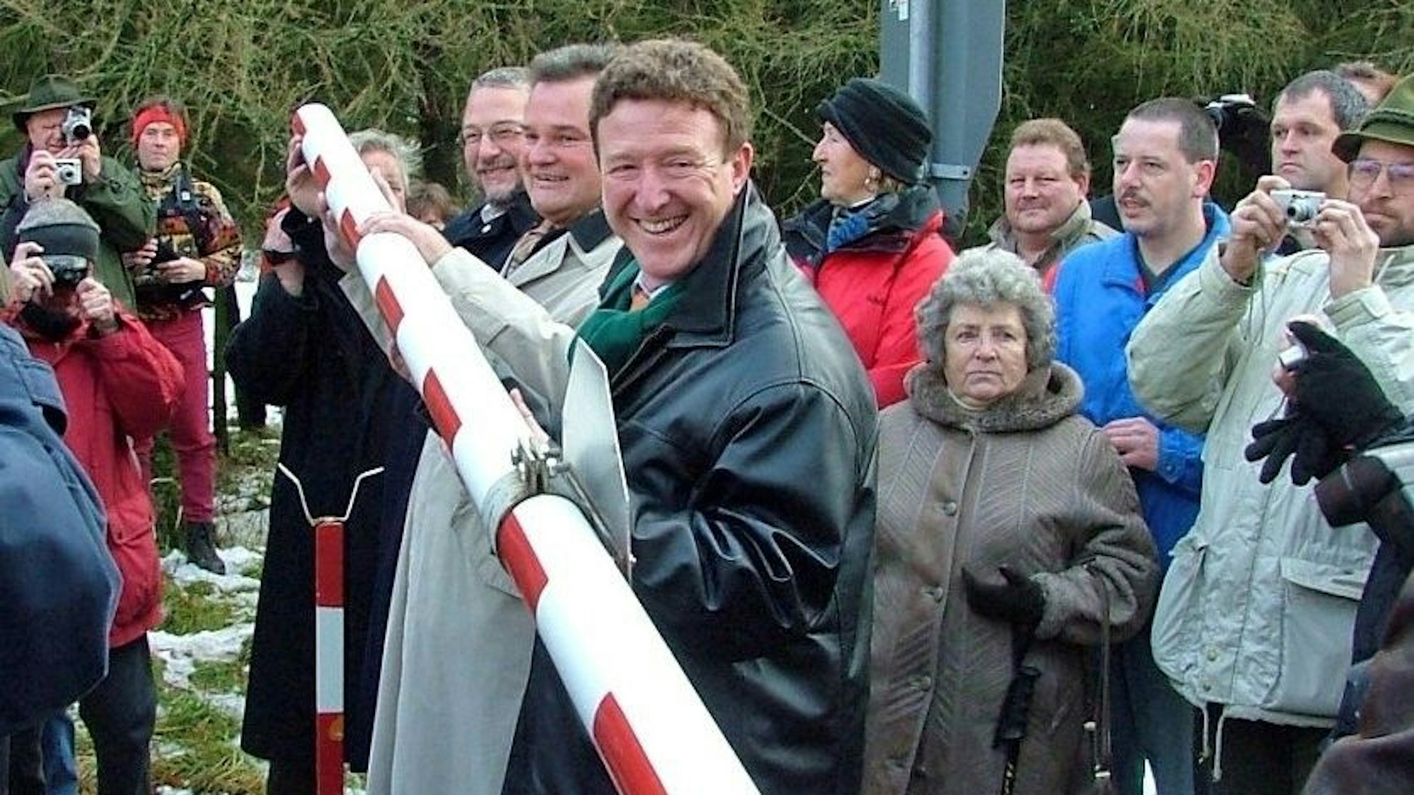 Drei Männer stehen an einer rot-weißen Schranke und heben sie hoch als Symbol, dass der Truppenübungsplatz Vogelsang wieder zivil ist. (Archivfoto)