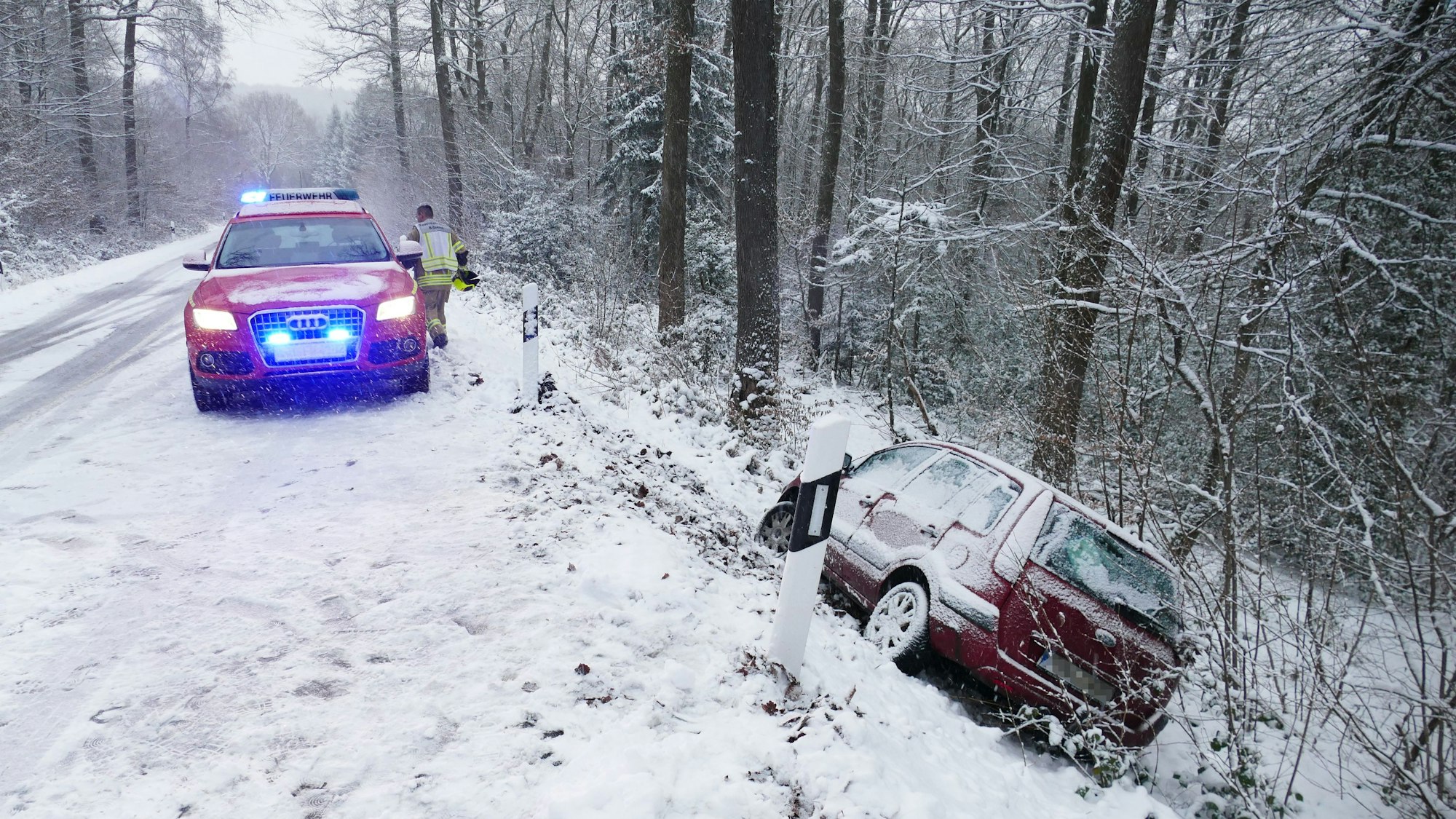 Ein Auto ist von der schneeglatten Fahrbahn abgekommen und liegt in einem Abhang im Wald.