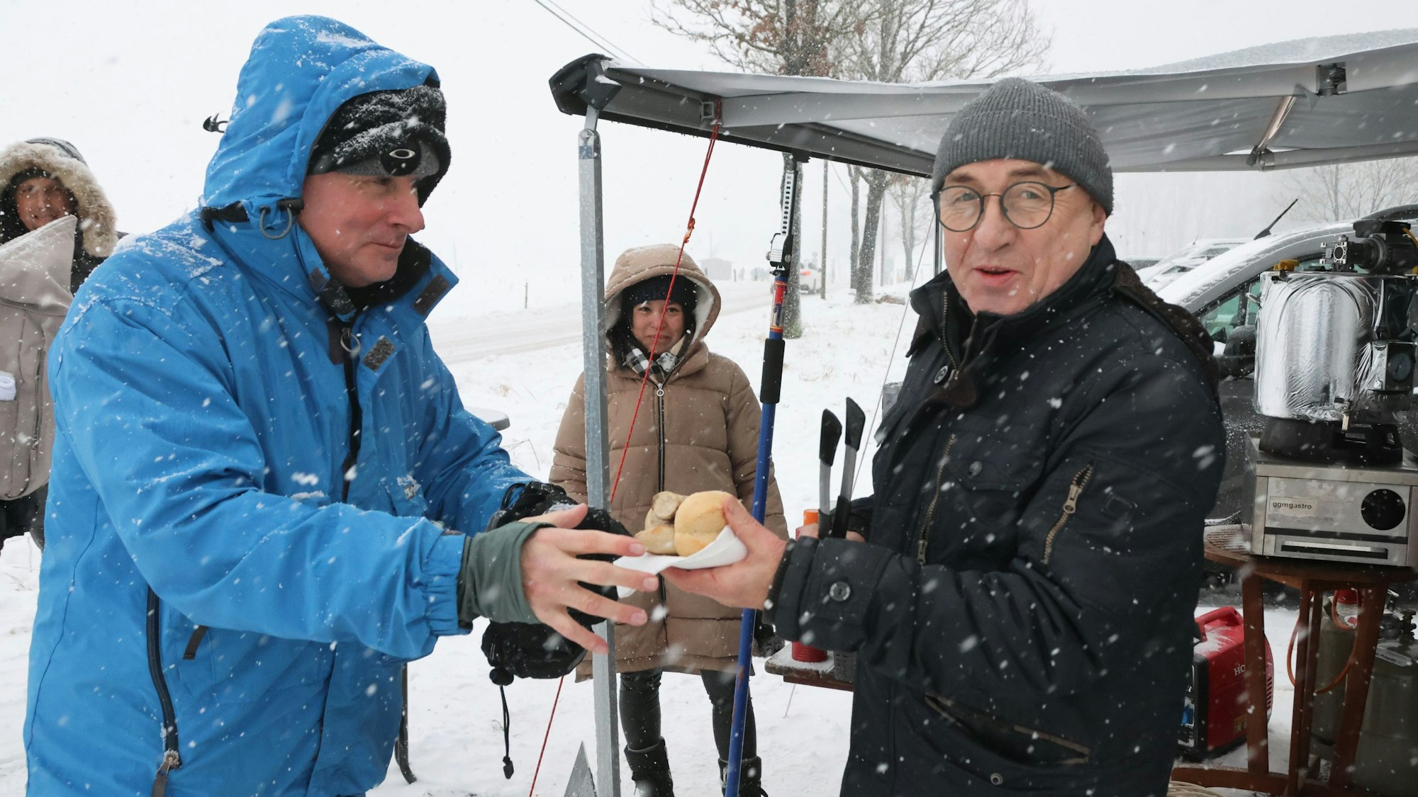 Das Foto zeigt, wie Bernhard Junge (rechts im Bild) Marc Dujardin eine Bratwurst reicht.