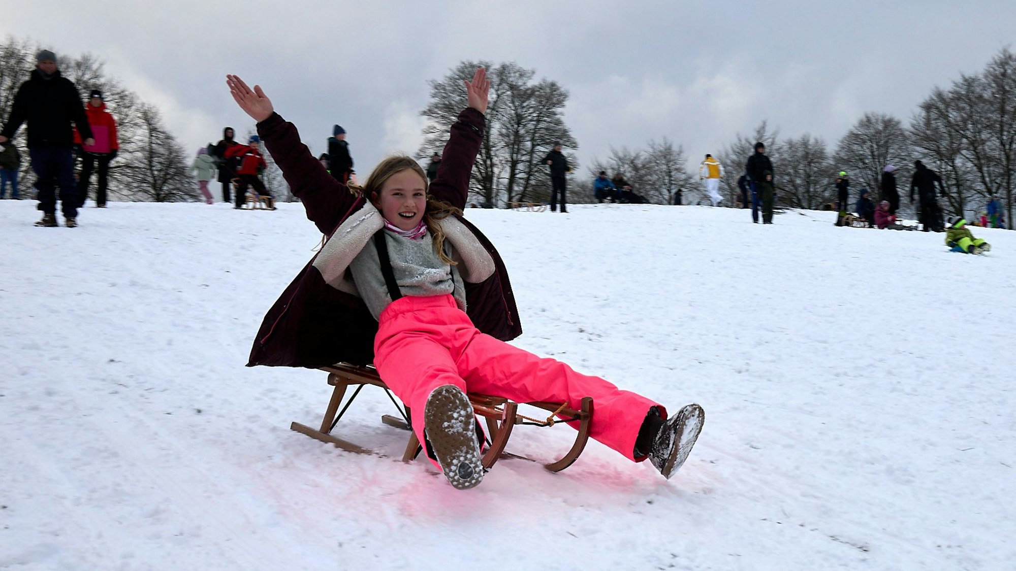 Ein Mädchen rodelt einen Hang hinunter und streckt die Arme zum Himmel.