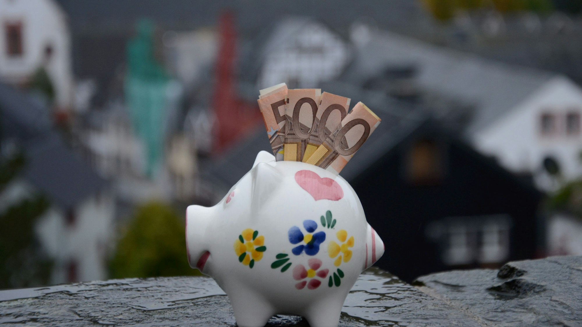 Das Bild zeigt ein Sparschwein mit vier eingerollten Geldscheinen im Schlitz.