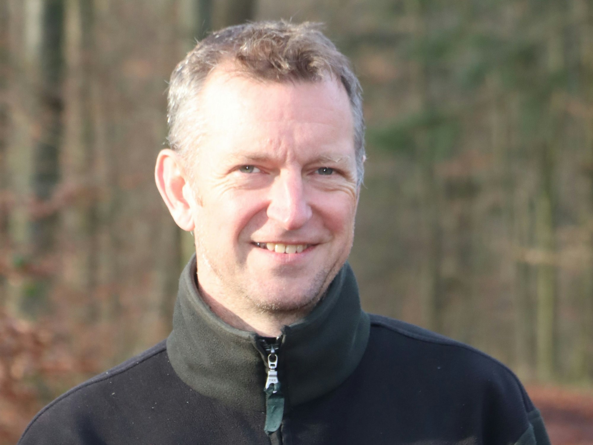 Ein Mann steht im Wald und lächelt.