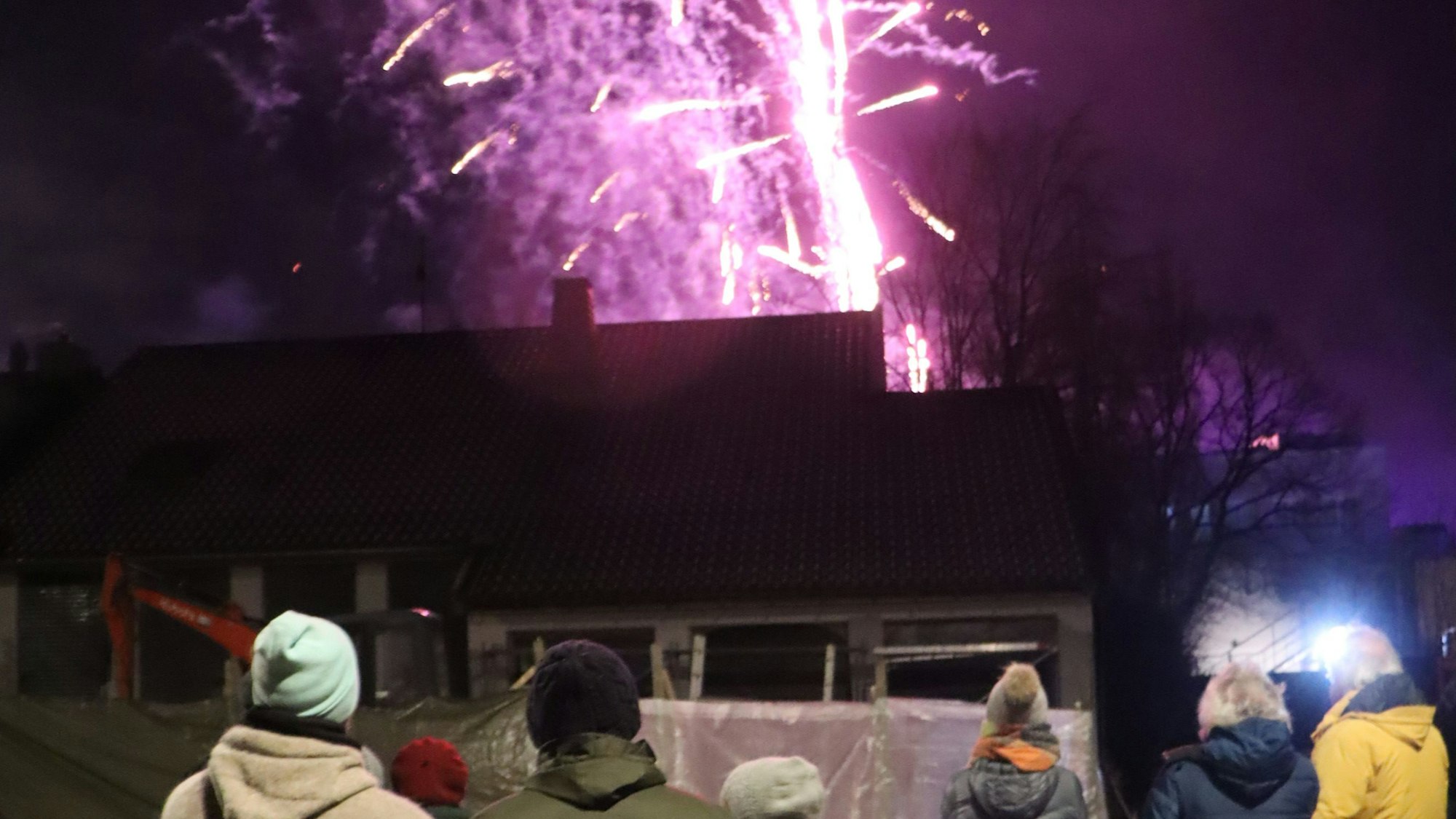 Zu sehen sind Menschen, die auf einen von Raketen erhellten Himmel schauen.