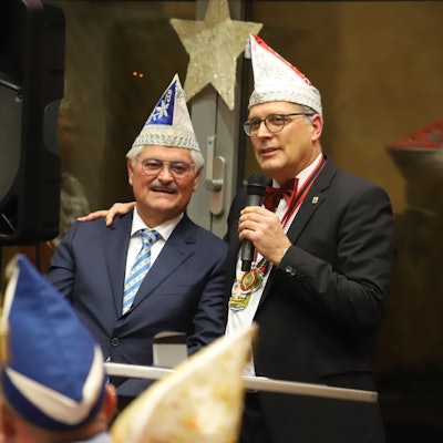 Reinhard Gotzen steht neben Bürgermeister Ulf Hürtgen. Der Bürgermeister hält ein Mikrofon in der linken Hand und hat seine rechte Hand auf Gotzens Schulter abgelegt.