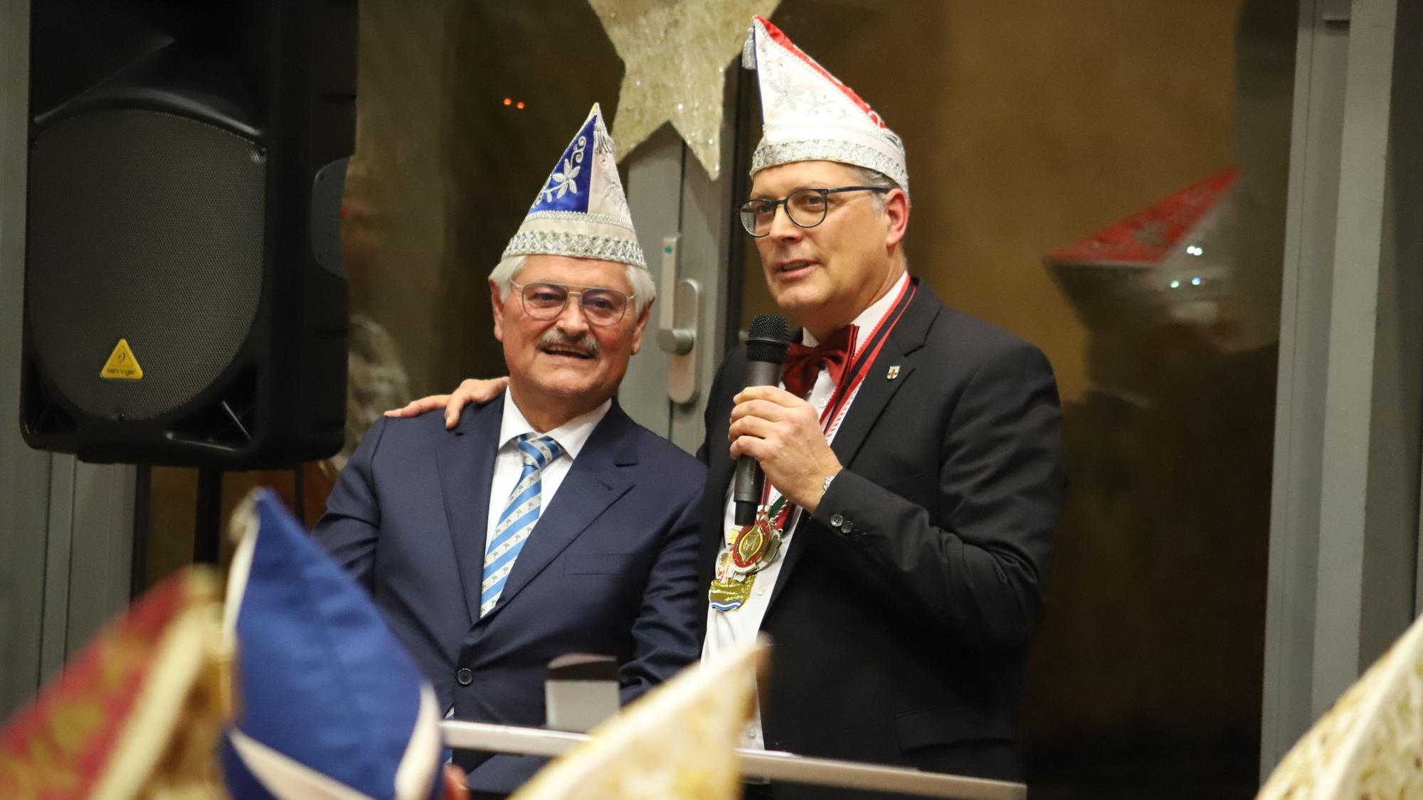 Reinhard Gotzen steht neben Bürgermeister Ulf Hürtgen. Der Bürgermeister hält ein Mikrofon in der linken Hand und hat seine rechte Hand auf Gotzens Schulter abgelegt.