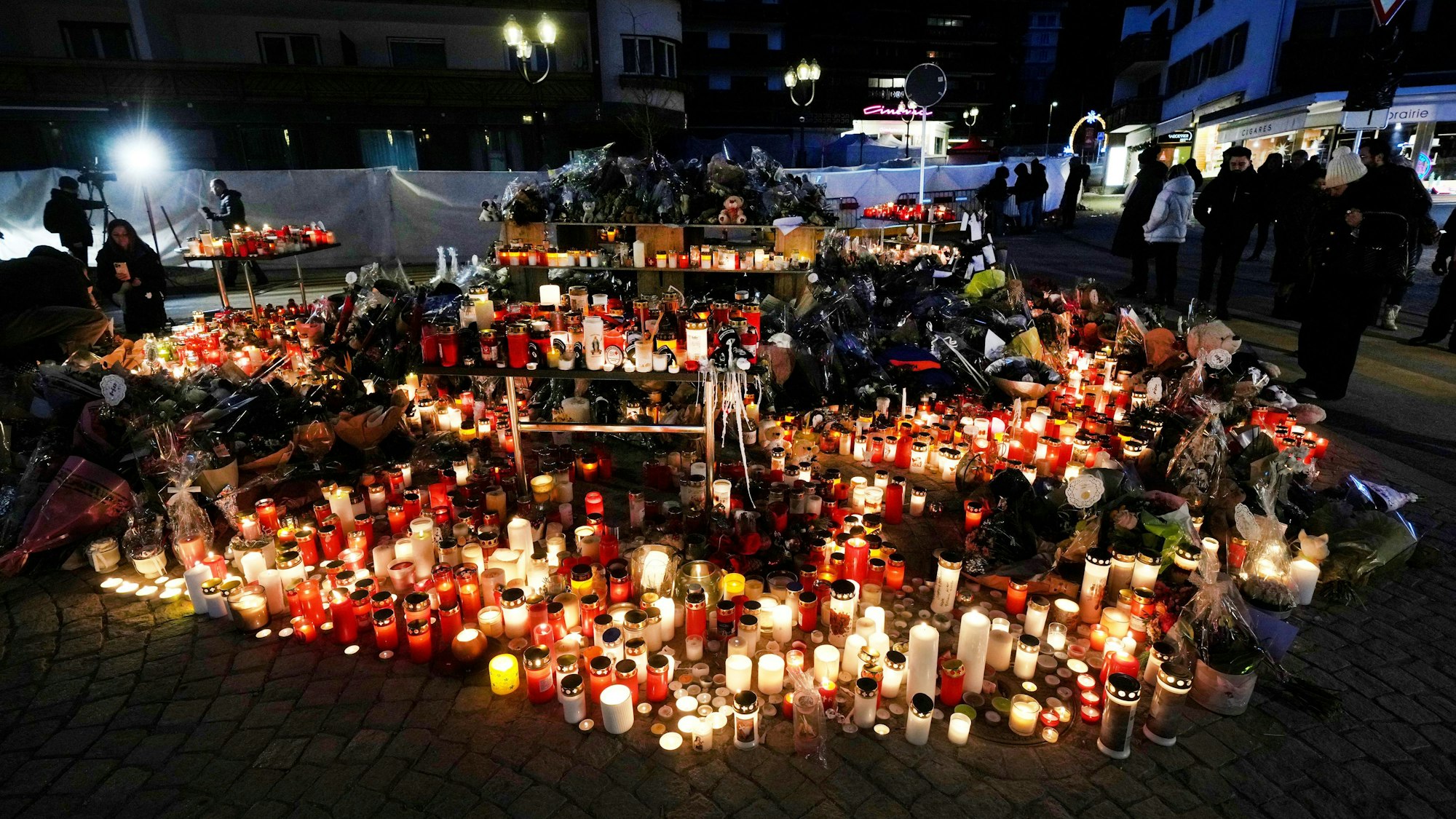 dpatopbilder - 04.01.2026, Schweiz, Crans Montana: Menschen zünden Kerzen an und legen Blumen vor der versiegelten Bar Le Constellation in Crans-Montana. Foto: Antonio Calanni/AP/dpa +++ dpa-Bildfunk +++