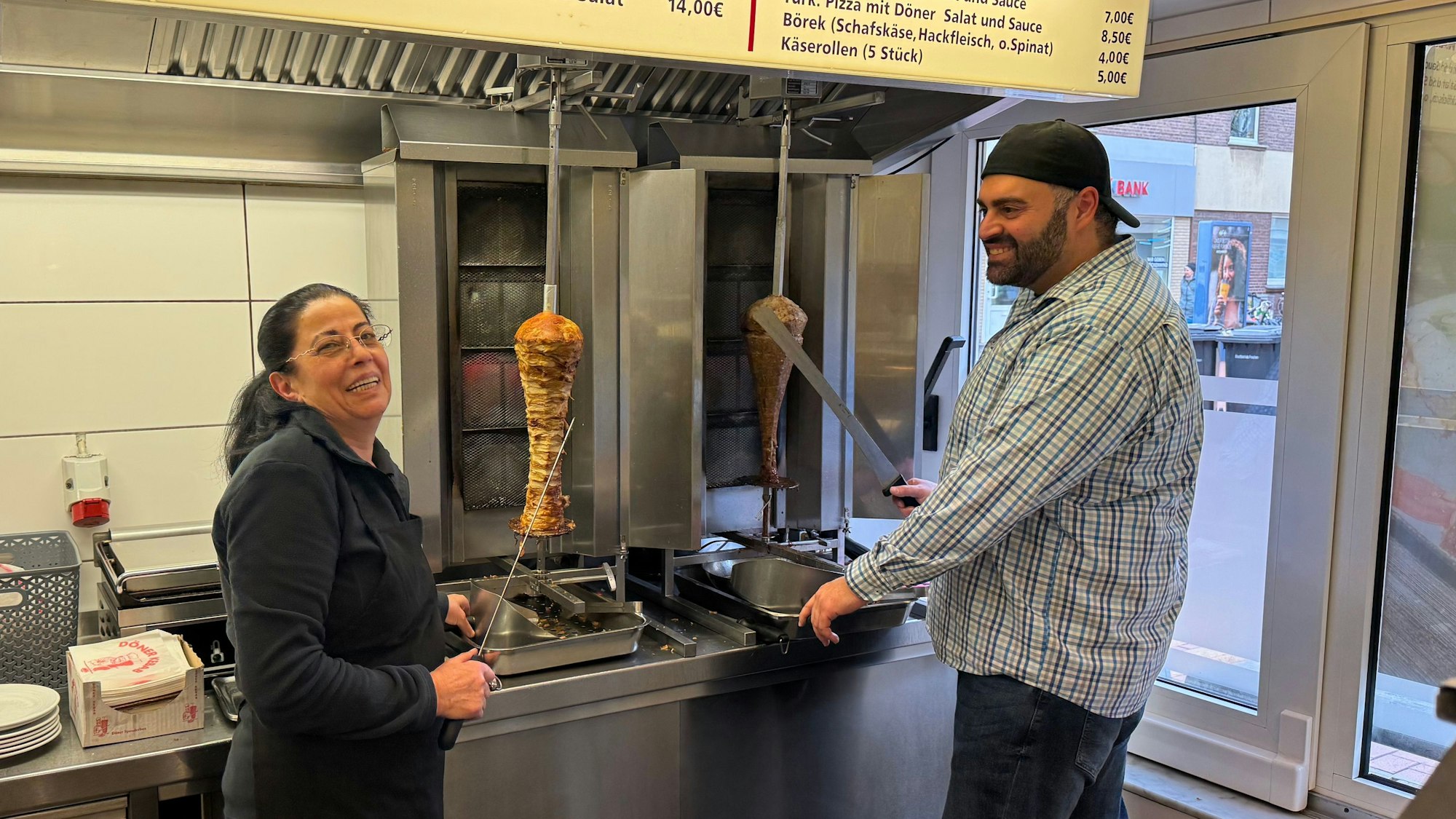Auf dem Bild ist eine Mutter mit ihrem erwachsenen Sohn vor zwei Dönerspießen zu sehen.