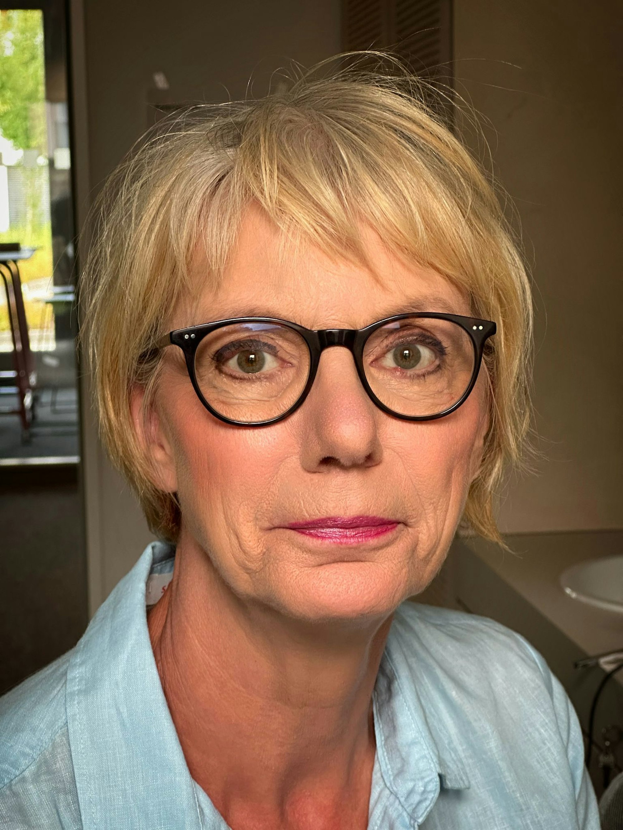 Eine blonde Frau mit kurzen Haaren und einer schwarzen Brille.