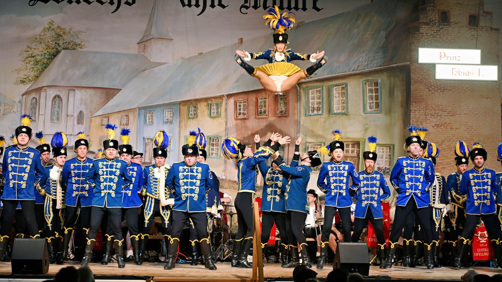 Männer in blauer Uniform stehen auf der Bühne und werfen ein Funkenmariechen in die Luft.