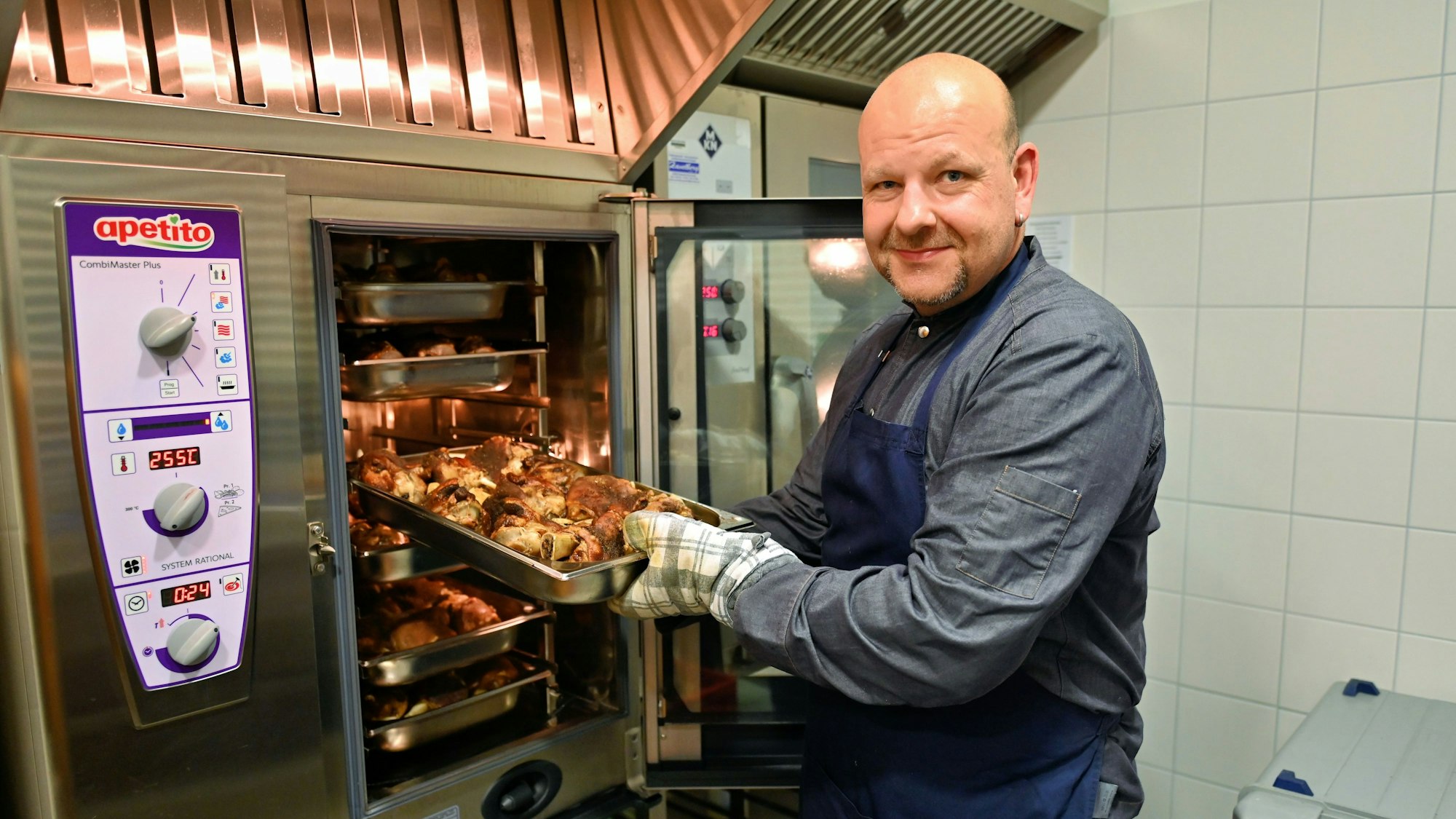 Christian Müller holt ein Blech mit Haxen aus dem Ofen.