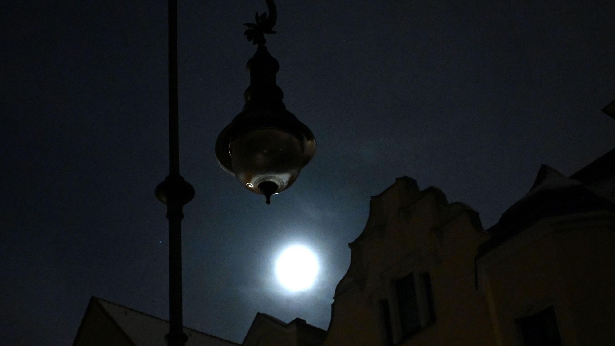 Eine dunkle Straßenlaterne in Berlin-Zehlendorf wird vom Mondlicht erhellt, im Hintergrund sind die Umrisse von Häusern zu sehen.