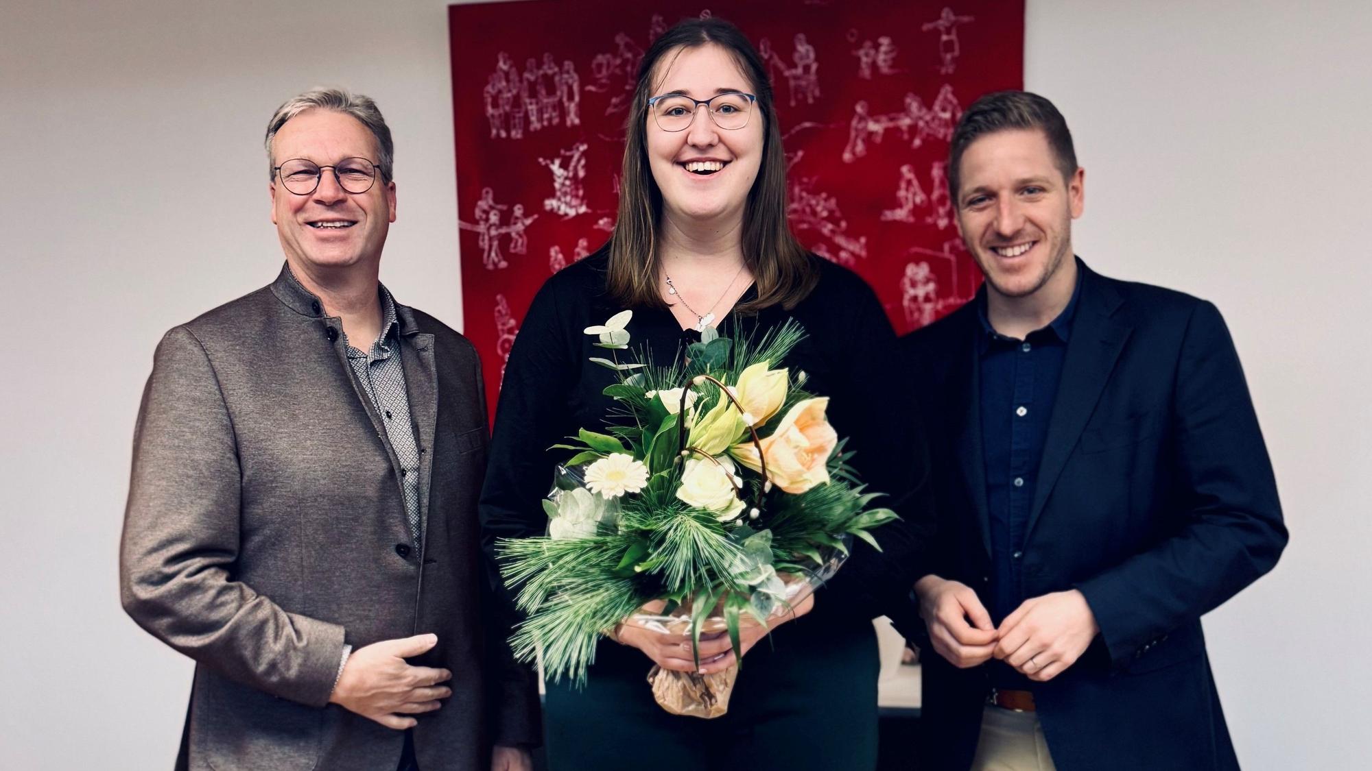 Hannah Bär hält einen Blumenstrauß und grinst in die Kamera. Sie wird von Landrat Markus Ramers (r.) und dessen Allgemeinen Vertreter Achim Blindert flankiert.