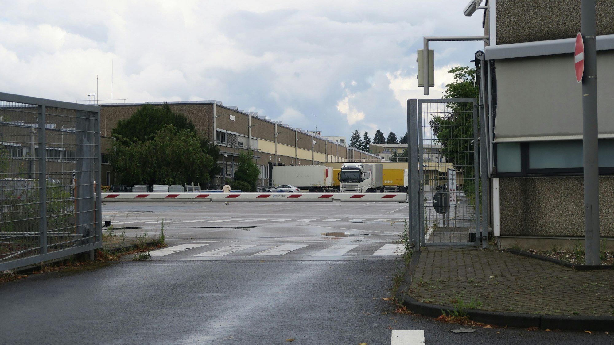 Hinter einem Schlagbaum ist der Betriebshof eines Firmengeländes zu sehen.
