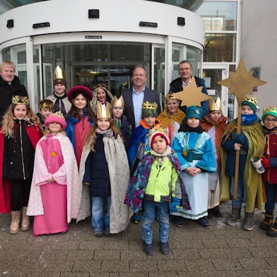 Die Sternsinger stehen mit dem Kaplan, dem Diakon und dem Landrat vor dem Eingang des Kreishauses.