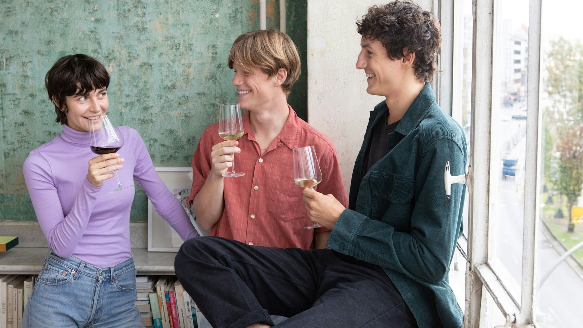 Drei Leute stehen mit Weingläsern in einem Zimmer.