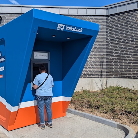 Zu sehen sind der blau-orange Pavillon und ein Kunde am Automaten.