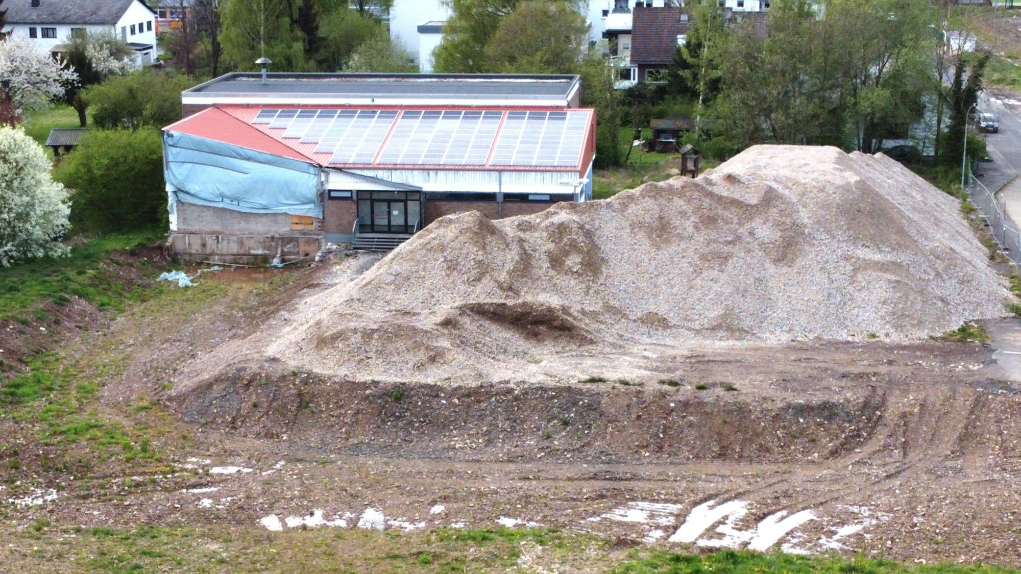 Blick auf die alte Turnhalle, vor der ein Schutthaufen liegt.