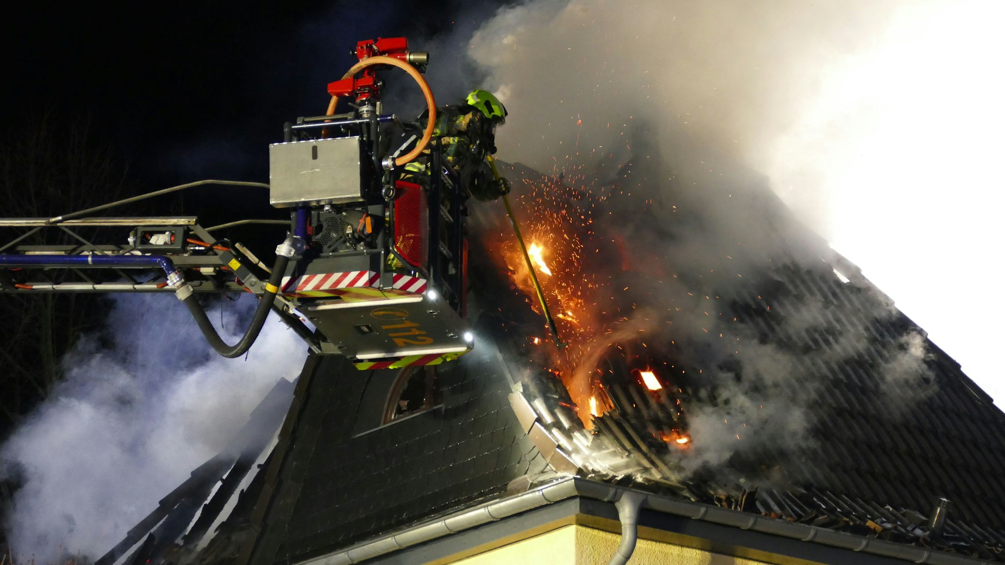 Mit einem Einreißhaken stößt der Feuerwehrmann Dachschindeln herunter