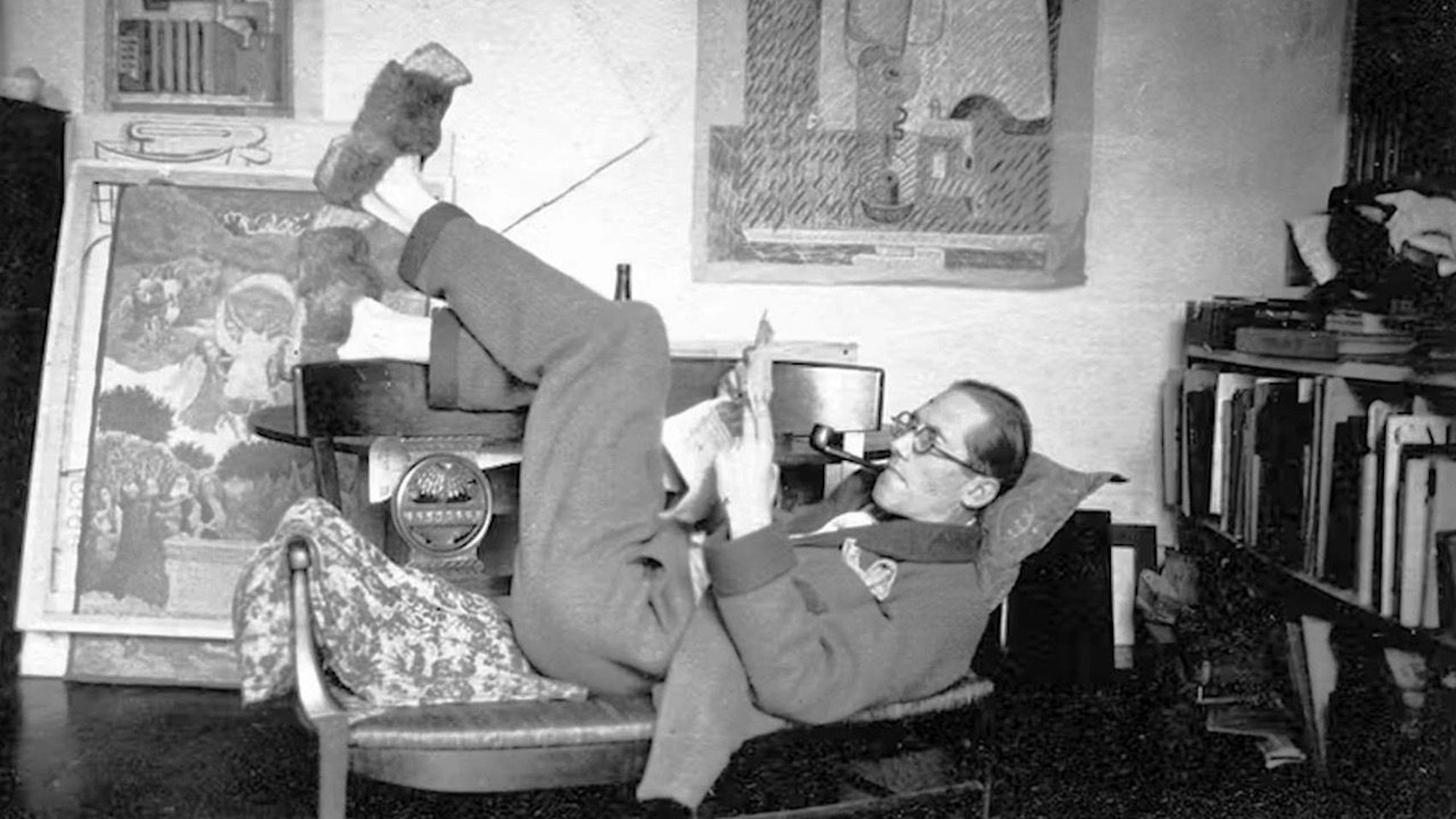 Le Corbusier liegt auf einer Bank mit den Beinen in der Luft.