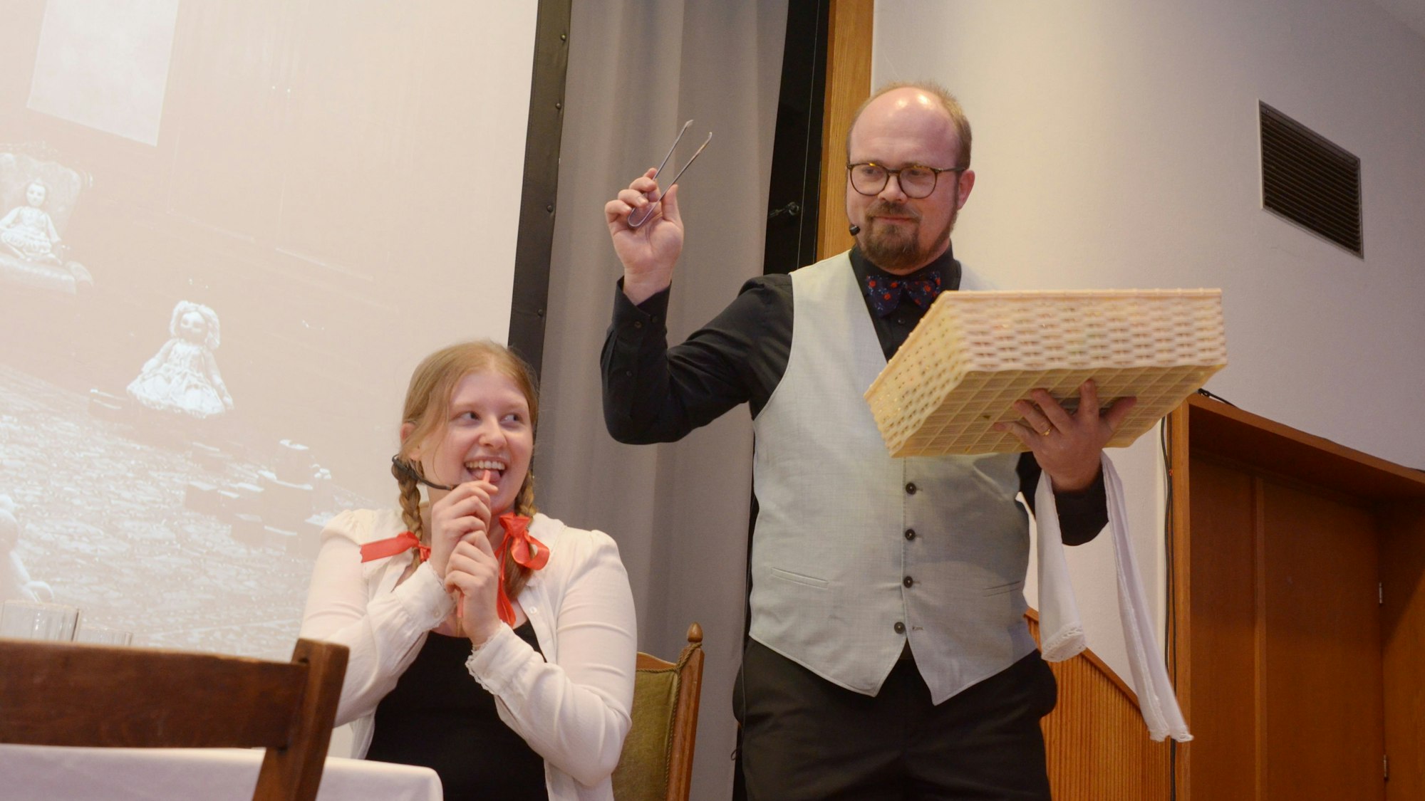 Magdalena Bork sitzt am Tisch, Gregor Weichsel steht in der Rolle des Butlers neben ihr.