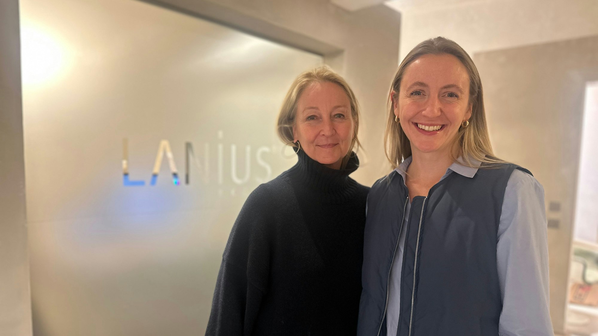 Ein Mutter-Tochter-Gespann steht vor einer milchigen Glaswand, auf der Lanius steht.