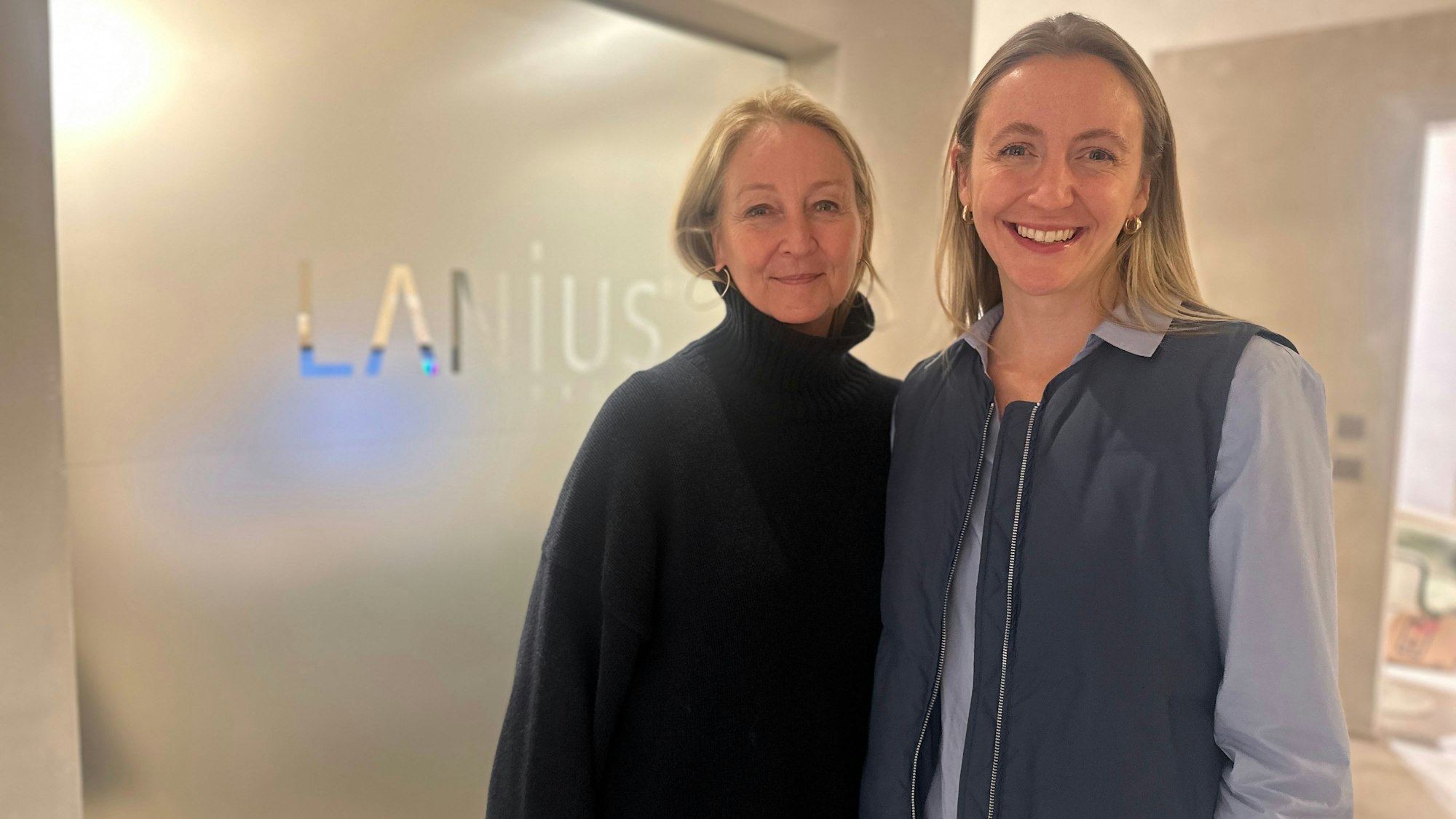 Ein Mutter-Tochter-Gespann steht vor einer milchigen Glaswand, auf der Lanius steht.