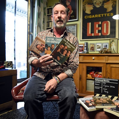 Ein Mann hält drei Bücher in die Kamera.